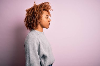 Kıvırcık saçlı, sıradan bir süveter giyen, rahat bir profil pozu veren, kendine güvenen gülümseyen güzel Afro-Amerikan kadın..