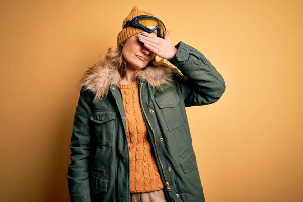 中年漂亮的金发滑雪者女人 穿着雪地运动鞋 戴着雪地护目镜 用手捂住眼睛 看起来严肃而忧郁 目光短浅 躲藏和拒绝的概念 — 图库照片