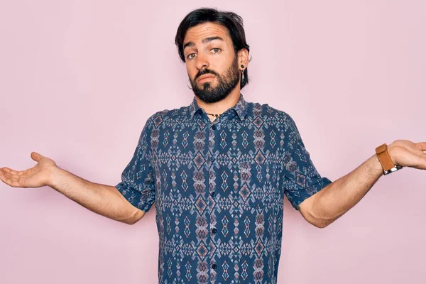 Pembe arka planda hippi tarzı giyinen yakışıklı, bohem bir adam. Kolları ve elleri havada, kafası karışmış bir ifade. Şüphe kavramı.