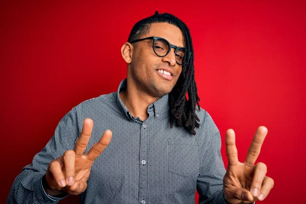 Rastgele gömlek ve gözlük takmış, gülümseyen ve parmaklarını zafer işareti yaparken gösteren genç, Afro-Amerikan bir adam. İki numara..