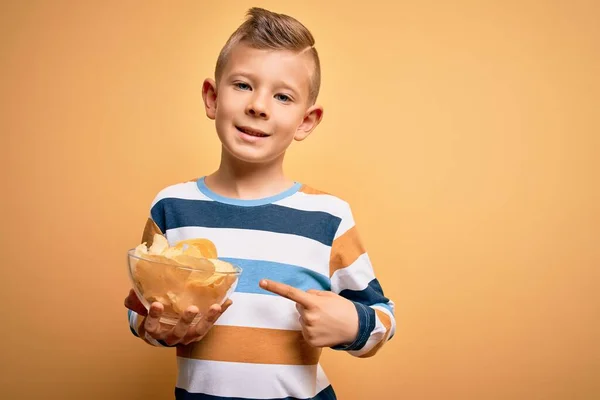 若いです小さなCaucasian子供食べるUnheathyポテトチップス上の黄色の背景非常に幸せなポインティングとともに手と指 — ストック写真