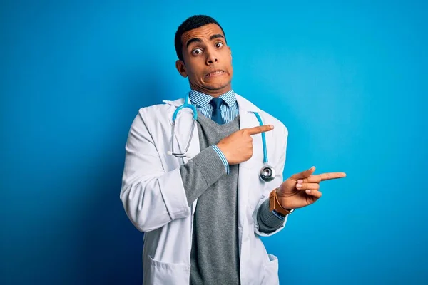 青い背景の上にコートと聴診器を身に着けているハンサムなアフリカ系アメリカ人医師手で心配し 緊張を脇に向けて 心配し 驚きの表情 — ストック写真