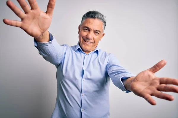 Middle age handsome grey-haired business man wearing elegant shirt over white background looking at the camera smiling with open arms for hug. Cheerful expression embracing happiness.