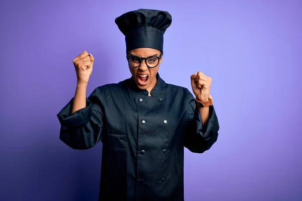 年轻的非洲女厨师身穿炊具制服 头戴紫色背景的帽子 怒气冲冲地举起拳头 怒气冲冲地大喊大叫 愤怒和好斗的概念 — 图库照片