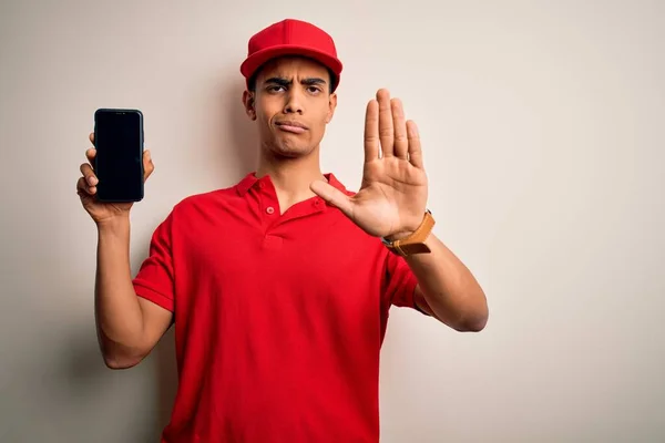 年轻英俊的非洲裔美国送货员手持智能手机 用张开的手展示屏幕应用程序 用严肃而自信的表情和防御手势做了个停车手势 — 图库照片