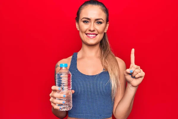 Jovem Mulher Loira Bonita Bebendo Garrafa Água Sobre Fundo Vermelho — Fotografia de Stock