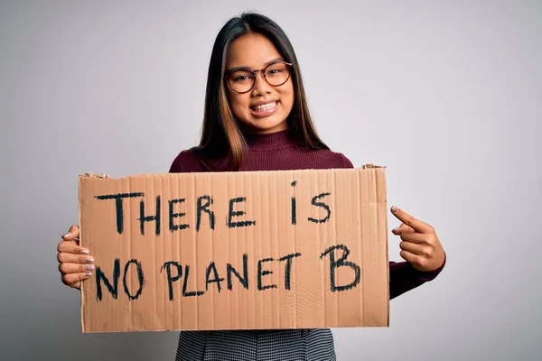 Young asian activist girl asking for environment holding banner with planet message very happy pointing with hand and finger