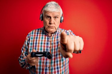 Oyun oynayan kıdemli beyaz oyuncu joystick ve kulaklıkla kamerayı işaret ediyor ve sen, el işareti, ön taraftan pozitif ve kendinden emin bir jest.