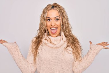 İzole edilmiş beyaz arka plan üzerinde dikilmiş, kollarını kaldırıp heyecanla haykıran, çılgın ve başarıyı kutlayan genç sarışın kadın. Kazanan konsept