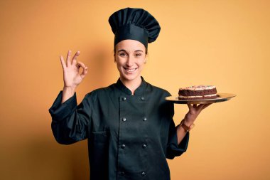 Fırıncı üniforması giyen genç ve güzel bir kadın ve pasta tepsisi taşıyan bir şapka. Parmaklarınla imzala, mükemmel bir sembol.