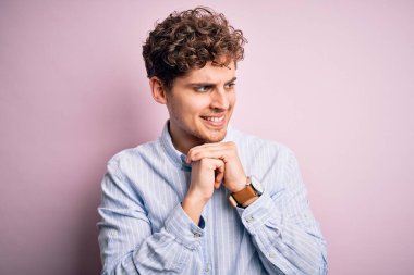 Sarışın, kıvırcık saçlı, beyaz arka planda çizgili tişörtlü, gergin ve heyecanlı, çenesi yana bakan genç bir adam.