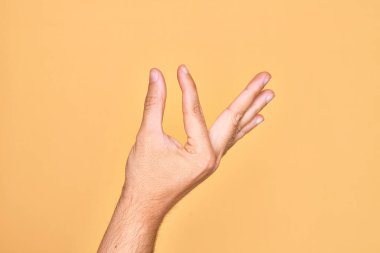 İzole edilmiş sarı arka plan üzerinde parmaklarını gösteren beyaz bir adamın eli. Görünmez bir şeyi alıp, parmaklarıyla uzayı gösteren bir nesneyi tutuyor.