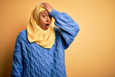 Genç Afrikalı Afro kadın, izole edilmiş sarı arka plan üzerine Müslüman başörtüsü takıyor. Hatayla el ele tutuşup şaşırıyor. Hatayı hatırla. Unuttum, kötü hafıza konsepti.