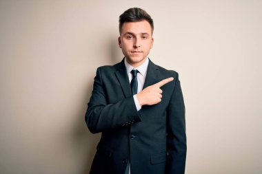 Zarif takım elbiseli ve kravatlı genç yakışıklı iş adamı izole edilmiş arka plan üzerinde el parmağı ile reklamını gösteriyor, ciddi ve sakin bir yüz.