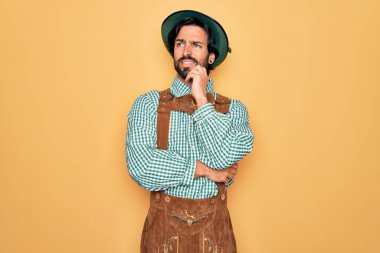 Almanya festivali için geleneksel Alman Ekim Festivali kıyafeti giyen genç yakışıklı bir adam. Elleri çenesinde soru sorarken, düşünceli bir ifade takınıyor. Gülen ve düşünceli bir yüz. Şüphe kavramı.