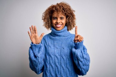 Beyaz arka plan üzerine balıkçı yaka kazak giyen güzel Afro-Amerikalı kadın altı numarayı gösterirken kendinden emin ve mutlu bir şekilde gülümsüyor..