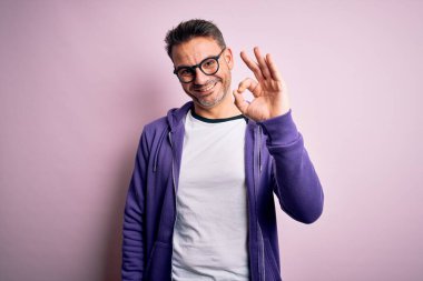 Pembe arka planda duran mor kazak ve gözlük takan yakışıklı genç adam el ve parmaklarıyla 