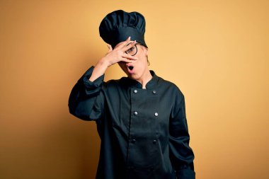 Güzel, esmer, aşçı üniforması giyen ve sarı arka planda şapka takan genç bir kadın. Şok olmuş bir şekilde yüzünü ve gözlerini kapatıyor. Utanmış bir ifadeyle parmaklarından bakıyor..