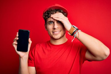 Kıvırcık saçlı, şapkalı, kırmızı arka planda akıllı telefon tutan genç bir teslimatçı. Elleri başının üstünde, utanç ve şaşkınlık dolu, sinirli ve hayal kırıklığına uğramış bir halde. Hata için korku ve üzüntü.