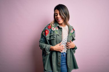 Moda kıyafetleri giyen genç ve güzel bir kadın. Manken, sokak tarzı giyiniyor. Pembe arka planda dikiliyor.