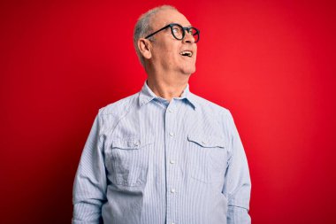 Orta yaşlı yakışıklı, beyaz, sıradan çizgili tişört giyen ve kırmızı arka planda gözlük takan yüzünde gülümseme, doğal bir ifade olan bir adam. Kendinden emin gülen.