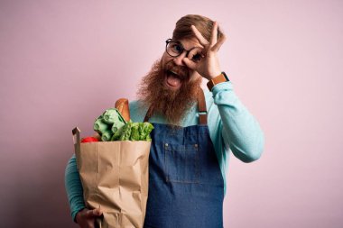 Kızıl saçlı İrlandalı süpermarket çalışanı, sakallı, önlüklü, elinde gülen yüzlü, taze bakkaliyeler tutan, el pençe divan duran, el pençe divan duran.