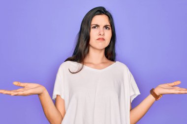 Genç, güzel, esmer bir kadın mor arka plan üzerine günlük beyaz tişört giyiyor. Hiçbir şeyden habersiz ve kolları açık, hiçbir fikri yok..