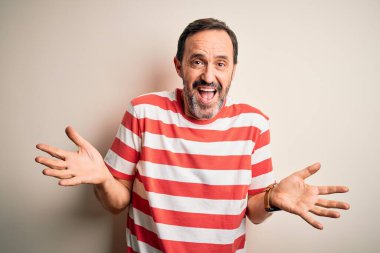 Sıradan çizgili tişört giyen orta yaşlı bir adam izole edilmiş beyaz arka plan üzerinde duruyor. Kolları ve elleri havada kafası karışmış bir ifade takınıyor. Şüphe kavramı.