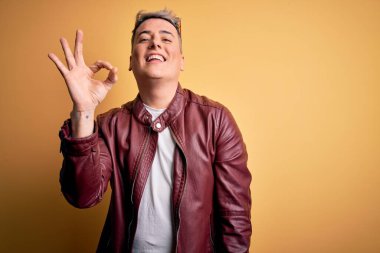 Sarı arka planda moda deri ceket ve güneş gözlüğü takan yakışıklı modern adam el ve parmaklarıyla 