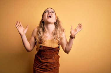 Tulum giymiş genç, sarışın bir kadın ve sarı arka planda dikilen Diadem deli deli deli bağırıyor ve agresif bir ifade ve kollarla bağırıyor. Hayal kırıklığı konsepti.