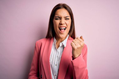 Genç, güzel, esmer bir kadın, pembe arka plan üzerinde dikiliyor kızgın ve kızgın. Öfkeyle bağırırken yumruğunu kaldırıyor. Öfke ve agresif kavram.