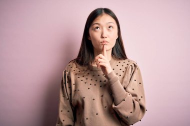 Pembe arka planda zarif süveter giyen genç, güzel Asyalı kadın şüpheye odaklanmıştı.