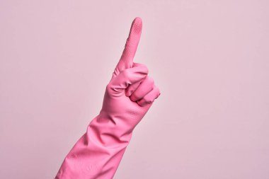 İzole edilmiş pembe arka plan üzerinde temizlik eldiveni olan beyaz bir gencin eli işaret parmağı kullanarak bir numarayı sayıyor, fikir ve anlayış gösteriyor.