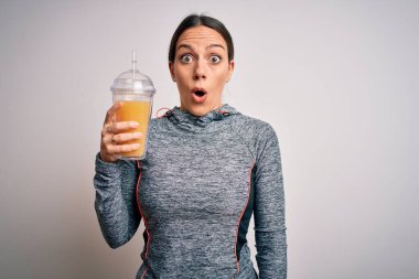 Spor kıyafetleri giyen, taze portakal suyu içen, şaşırmış ve korku ifadesinden korkan genç bir fitness kadını.