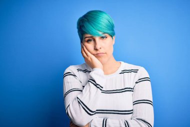 Mavi saçlı, sıradan bir süveter giyen genç ve güzel bir kadın stüdyoda dikilip kollarını kavuşturup depresyondan sıkılmış ve yorgun göründüğünü düşünüyor..