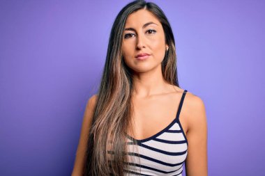 Genç, güzel bir kadın, mor izole edilmiş arka plan üzerinde günlük çizgili kıyafet giyiyor ve yüzünde ciddi bir ifade var. Basit ve doğal bir şekilde kameraya bakıyorsun..