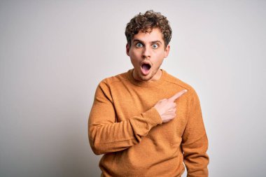 Sarışın, kıvırcık saçlı, beyaz arka plan üzerine günlük süveter giyen genç ve yakışıklı bir adam..