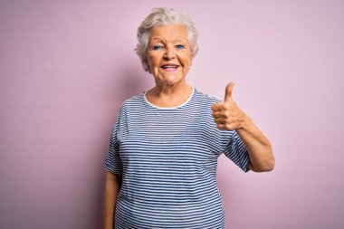 Son sınıftaki güzel, gri saçlı kadın pembe arka plan üzerine günlük tişörtler giyip el hareketleriyle mutlu mesut selam veriyor. Kameraya bakıp başarıyı gösteren ifade onaylanıyor.