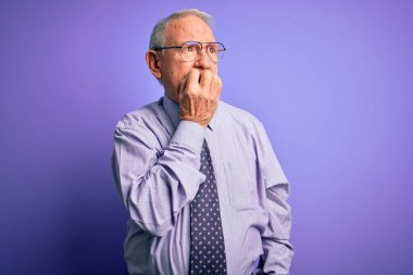 Mor izole edilmiş arka planda duran gözlüklü, gri saçlı yaşlı iş adamı elleri ağız yiyen tırnaklarla gergin ve stresli görünüyor. Endişe sorunu.