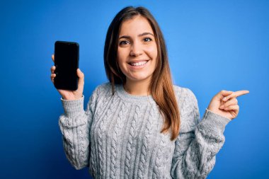 Mavi izole edilmiş arka planda boş akıllı telefon ekranı gösteren genç bir kadın.