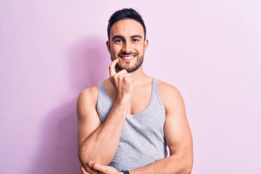 Sakallı, pembe arka planda kolsuz tişört giyen, kolları çapraz ve çenesi açık kameraya bakarak gülümseyen yakışıklı bir genç. Olumlu düşünüyorum..