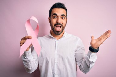 Sakallı, pembe kanser kurdelesi takan genç yakışıklı adam mutlu ve heyecanlı, kazanan yüz ifadesi zaferi büyük bir gülümsemeyle kutluyor ve ellerini kaldırıyor.
