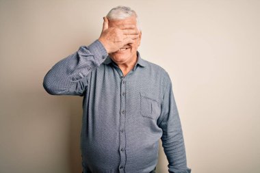 Üst düzey yakışıklı beyaz gömlekli adam izole edilmiş beyaz arka planda duruyor. Gülümsüyor ve elleri yüzünde şaşkınlıktan gözleri kapayarak gülüyor. Kör kavram.
