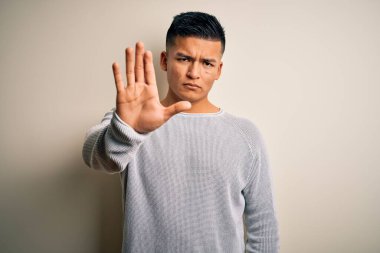İzole edilmiş beyaz arka planda dikilen ve avucunun içi gibi şarkı söylemeyi kesen gündelik süveter giyen genç, yakışıklı Latin adam. Yüzünde olumsuz ve ciddi bir jest olan uyarı ifadesi.