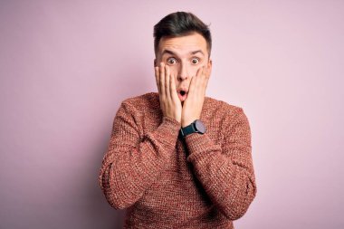 Pembe soyutlanmış arka plan üzerine sıradan bir kazak giyen yakışıklı beyaz bir adam korkmuş ve şok olmuş, şaşırmış ve şaşırmış bir yüz ifadesi takınıyor.