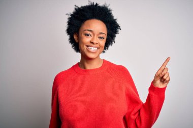 Kıvırcık saçlı, kırmızı kazaklı, yüzünde kocaman bir gülümseme olan, eli kameraya bakan güzel Afro-Amerikan bir kadın..