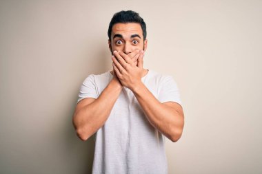 Young handsome man with beard wearing casual t-shirt standing over white background shocked covering mouth with hands for mistake. Secret concept.
