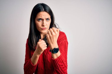 Mavi gözlü genç esmer kadın izole edilmiş beyaz arka plan üzerine günlük süveter giyiyor. Yumruk savunma hareketleriyle dövüşmeye hazır, kızgın ve üzgün yüzlü, sorundan korkan.