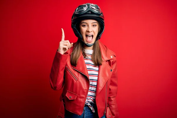 若い美しいブルネットのオートバイのヘルメットと赤いジャケットを身に着けているオートバイの女性は 成功したアイデアで指を指しています 興奮し 第一番 — ストック写真