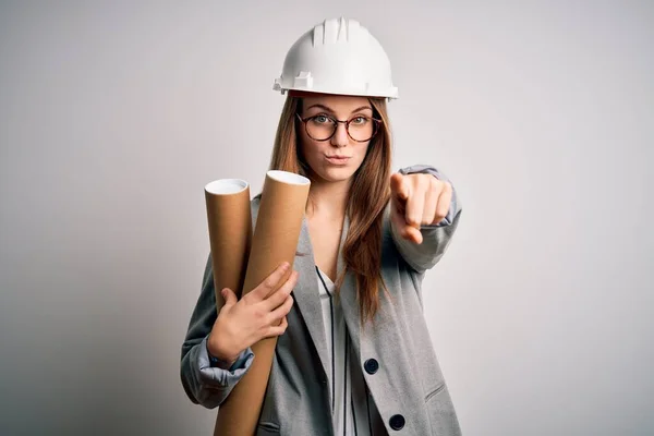 年轻美丽的红头发女建筑师 戴着眼镜 戴着安全帽 手里拿着设计图 手指着相机 正面是积极自信的手势 — 图库照片